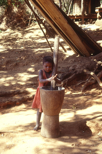 Photo of little girl grinding maize with tools made from protected area resources