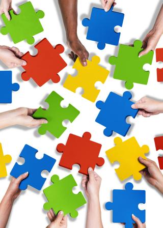 red, yellow, blue and green puzzle pieces with hands holding pieces toward center (shutterstock:213471511 (C) rawpixel)