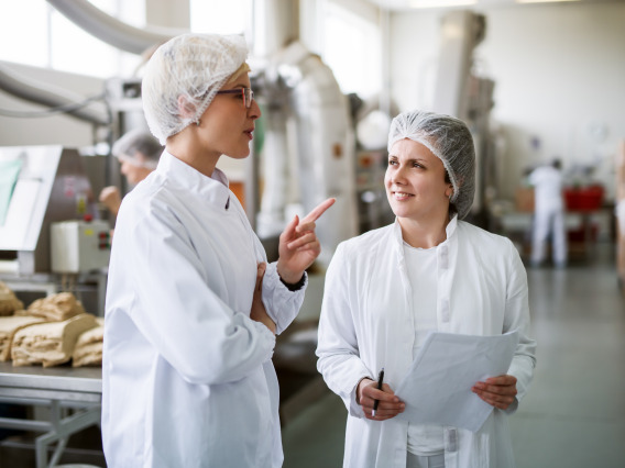 Two people wearing lab coats and hair protectors in a food processing lab.