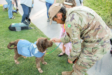 Woman in army uniform leaning over to pet her dog that is wearing a denim outfit